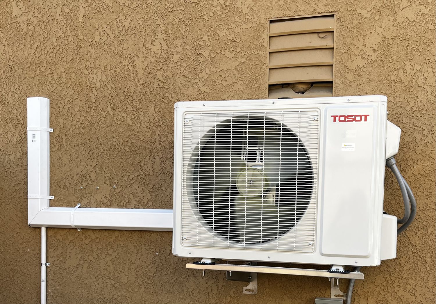 Wall-bracket mounted mini-split condenser on a stucco wall